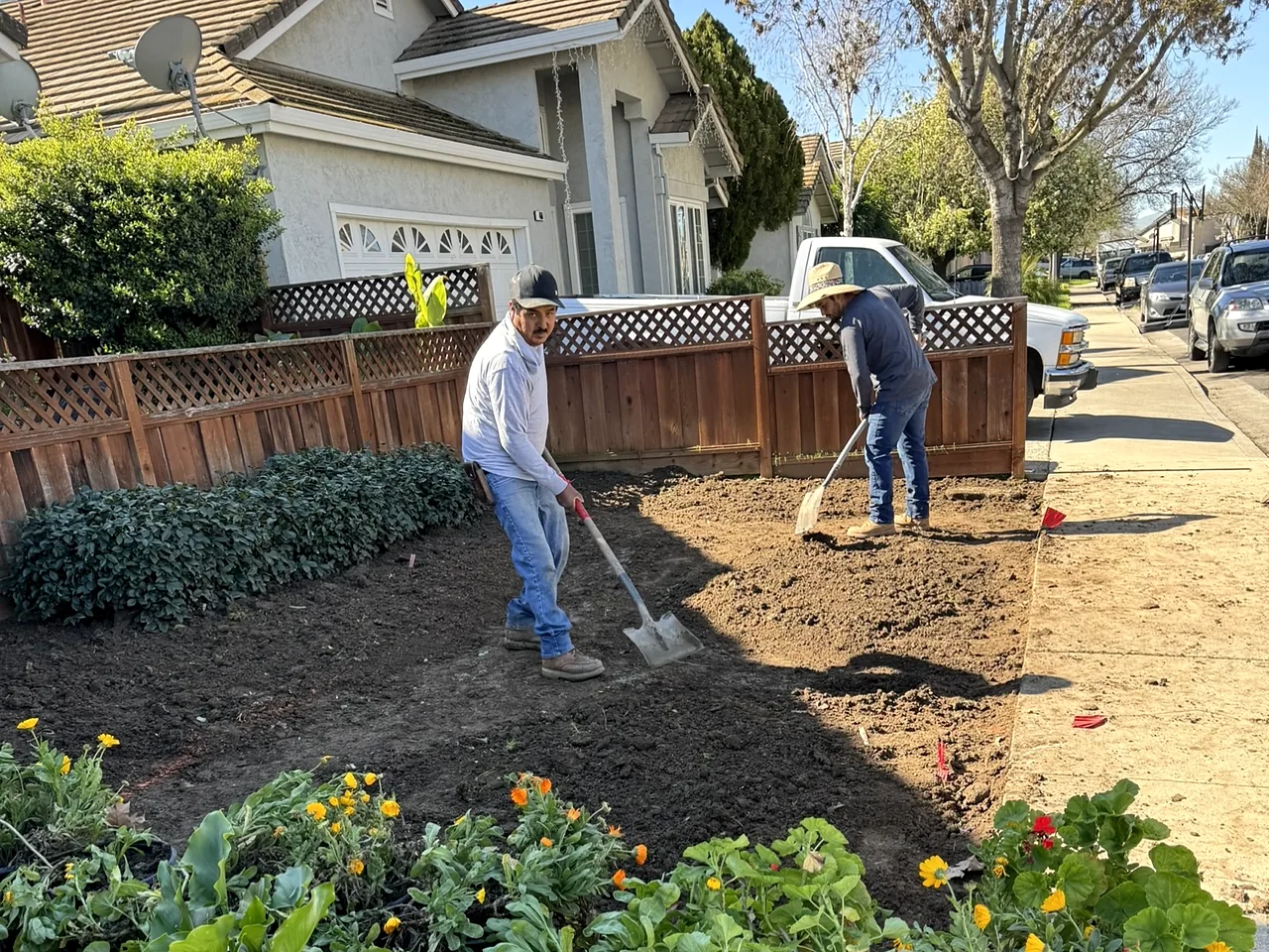 Crew turning the soil out front with flats of new plants waiting on the sidewalk