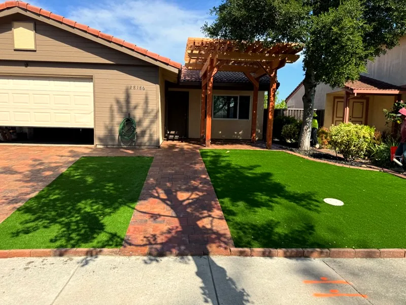 Front yard after: red paver driveway and walk with artificial turf under a new wood pergola