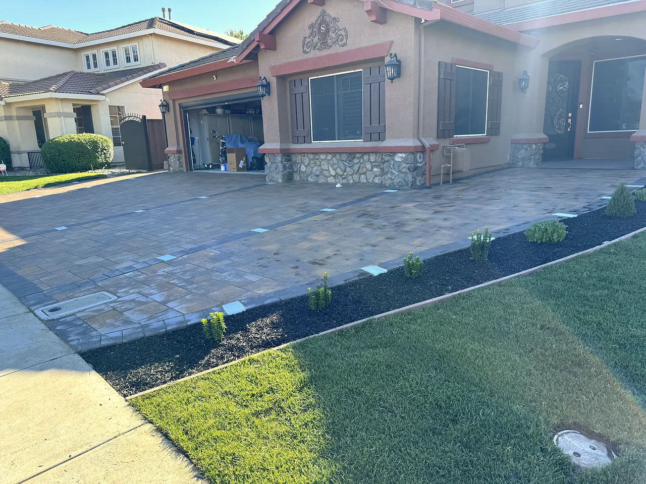 The same house after: a wide paver driveway, mulch bed with new shrubs and fresh lawn