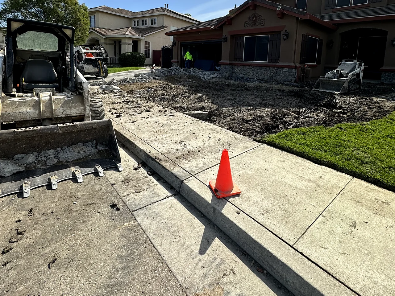 Tear-out day: skid steers clearing the old front yard of a two-story house